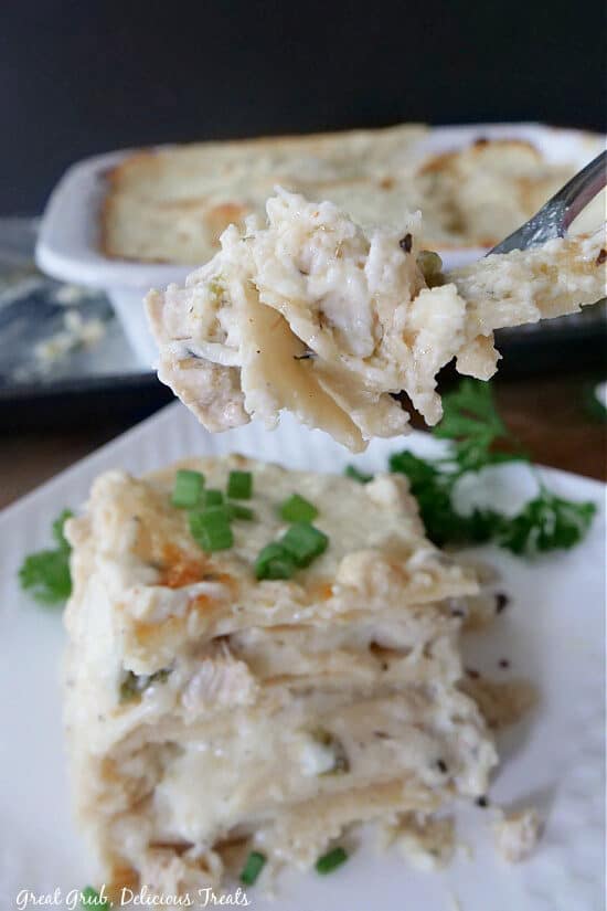 A bite of chicken enchiladas on a fork above a white plate with a serving on it.