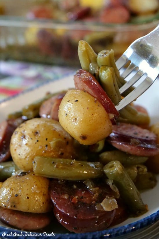 Sausage Green Bean Potato Casserole is a delicious casserole side dish, full of sausage, green beans and potatoes. A fork filled with a bite of potato, sausage and green beans on it.