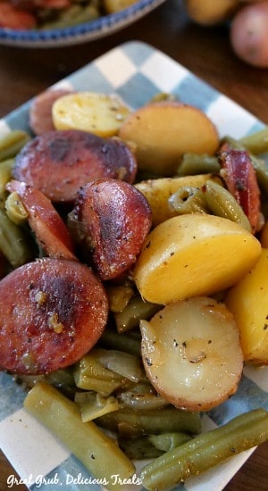 Sausage Green Bean Potato Casserole has delicious sausage kielbasa, green beans, baby potatoes and baked until tender. A light blue and white checkered plate with a serving of potatoes, green beans and sausage on it.
