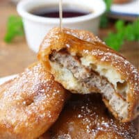 Three pancake sausage bites on a white plate with syrup being drizzled oven the top.