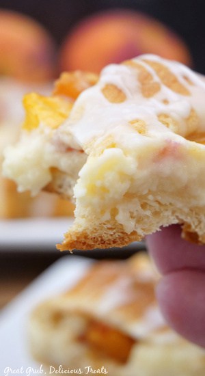 A peach pastry being held up with a bite taken out of it.