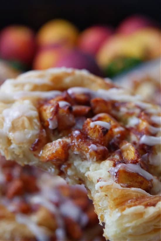 A close up of a peach cream cheese puff pastry with a bite taken out of it.