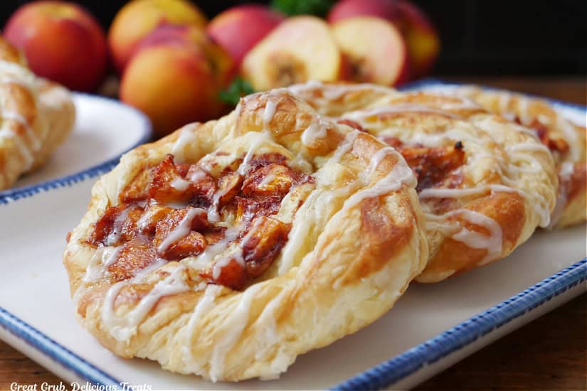 A horizontal photo of a white plate with blue trim filled with three peach puff pastries on it.