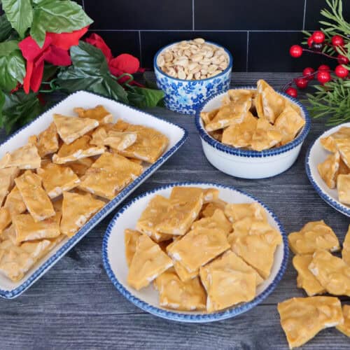 A grey surface with four white plates with blue trim filled with peanut brittle.