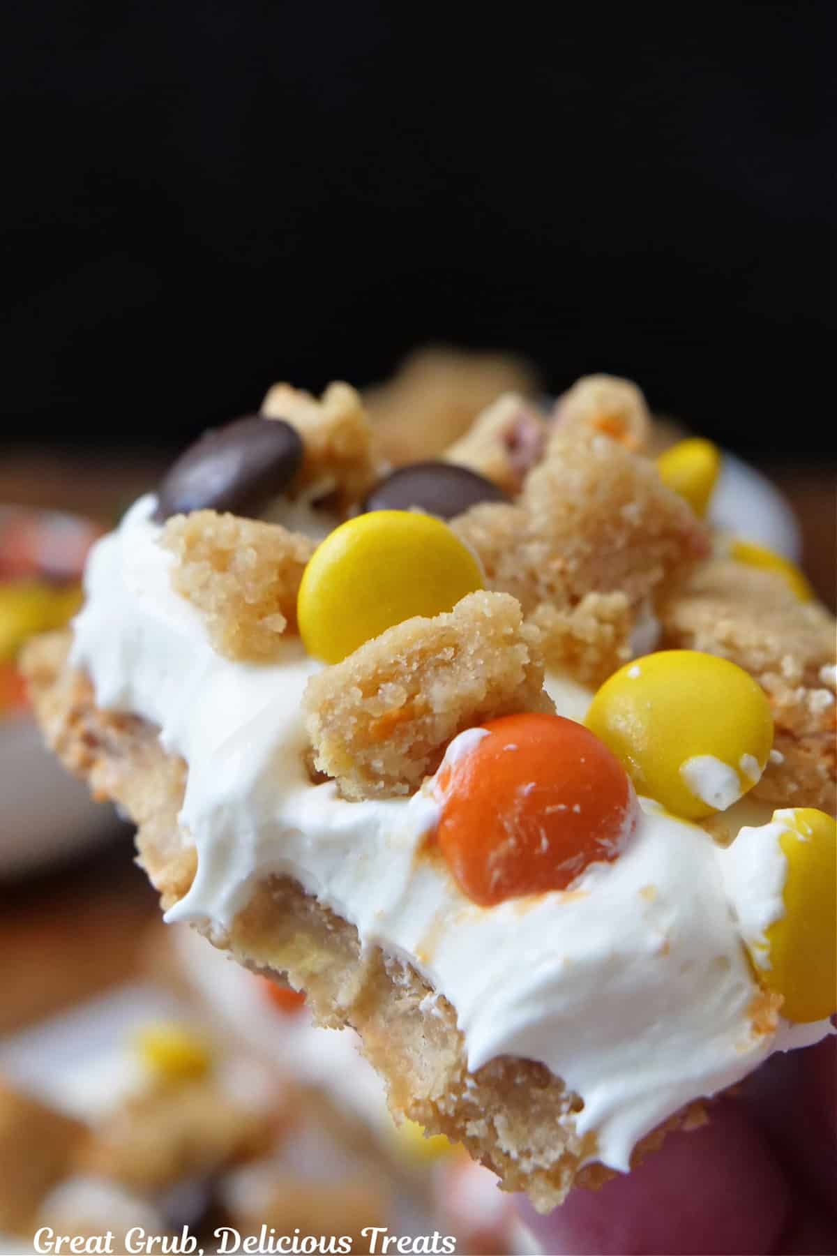 A serving of a cookie with cream cheese layer and crumbled cookies and Reese's pieces on top.