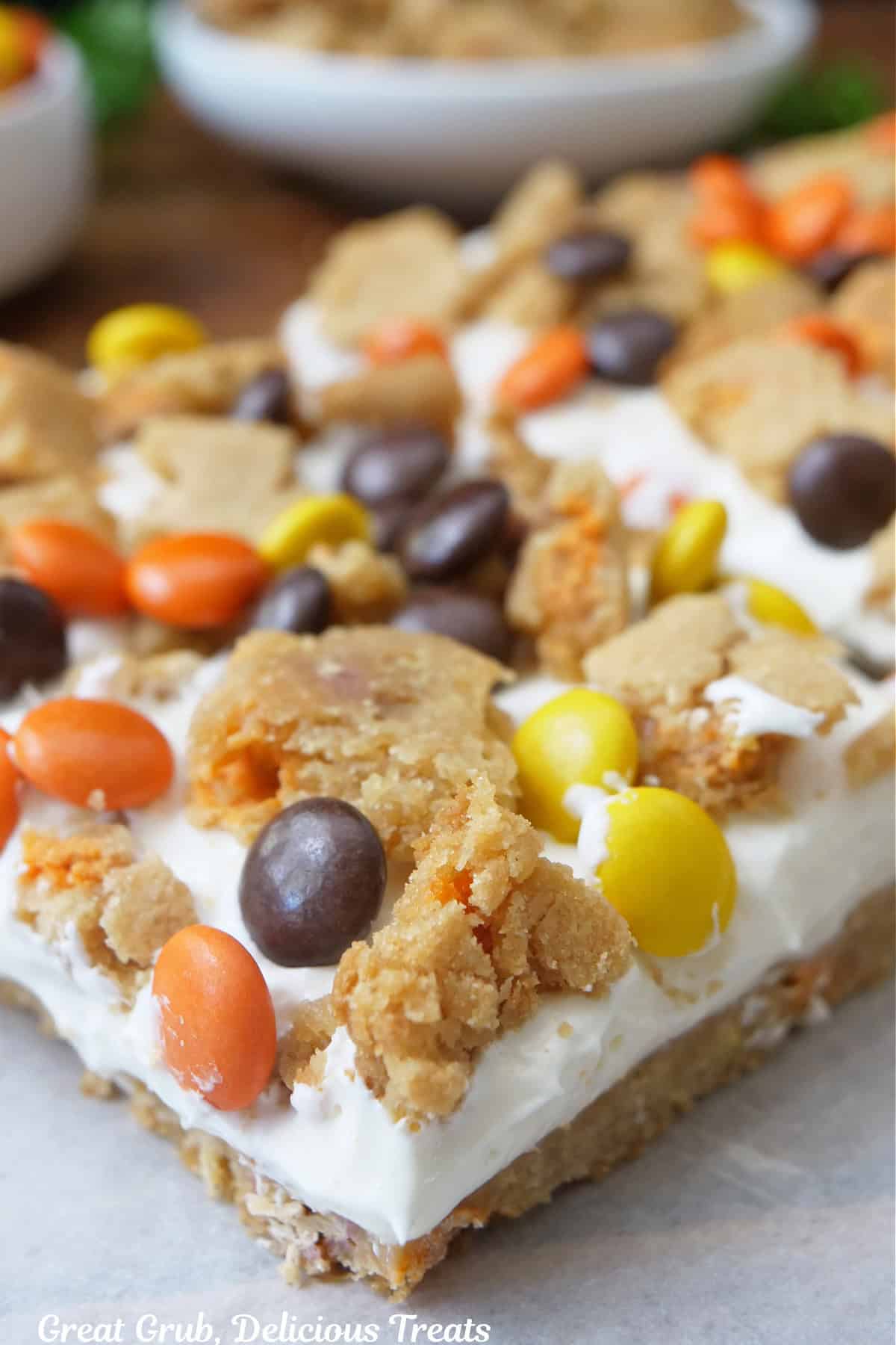 A piece of a square cookie with a cream cheese layer and cookie and candy pieces on top.