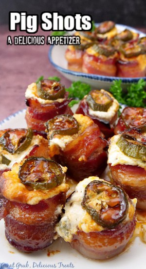 Two white plates with blue trim with bacon wrapped sausages with cream cheese mixture in them and topped with a jalapeño.