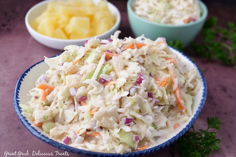 A white bowl with blue trim with a serving of coleslaw in it with two other bowls in the background.