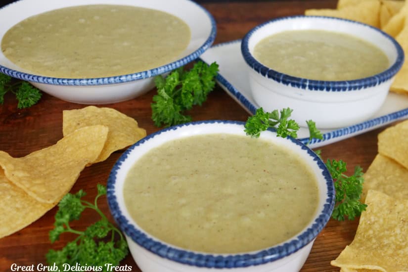 A wood surface with three bowls with blue trim filled with poblano cream sauce.