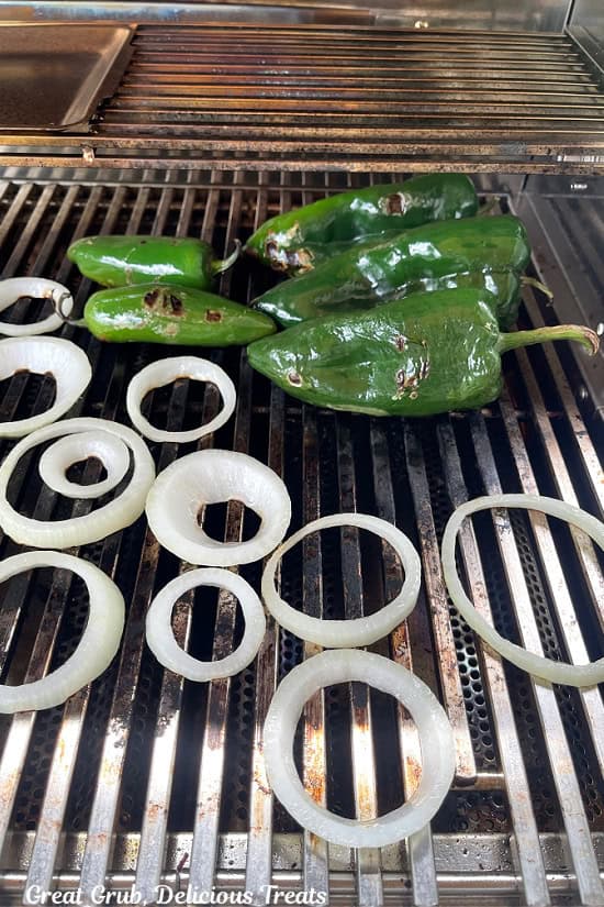 Poblano and jalapeno peppers, and onion are on the grill being roasted.