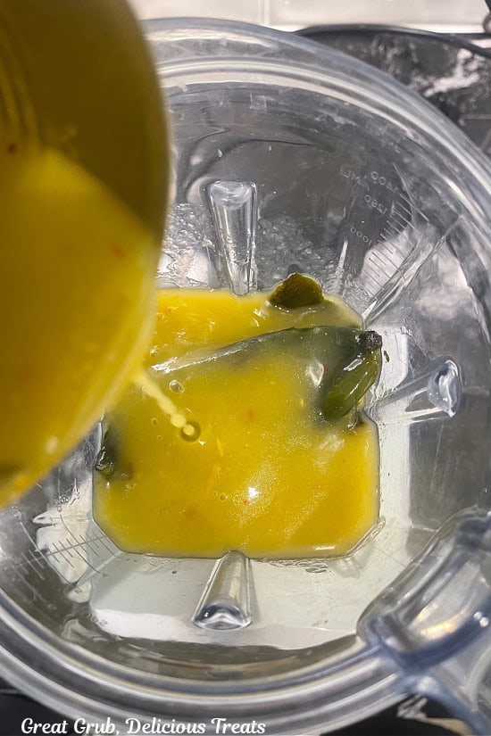 Enchilada sauce is added to a blender on top of the peppers.