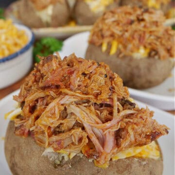 A white plate with a baked potato topped with pulled pork.