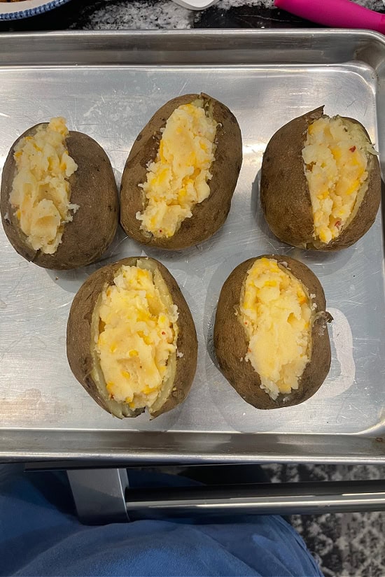 Five baked potatoes on a silver baking sheet after being stuffed with the potato cheese mixture.