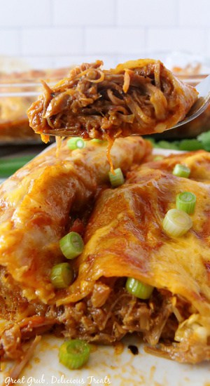 Two enchiladas on a white plate with a bite of enchilada on a fork.