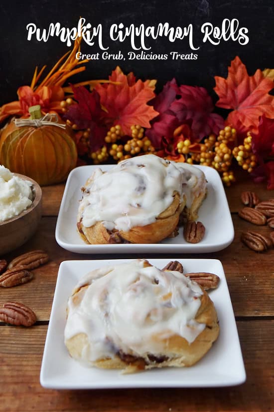 A wood surface with pumpkin cinnamon rolls on white square plates.