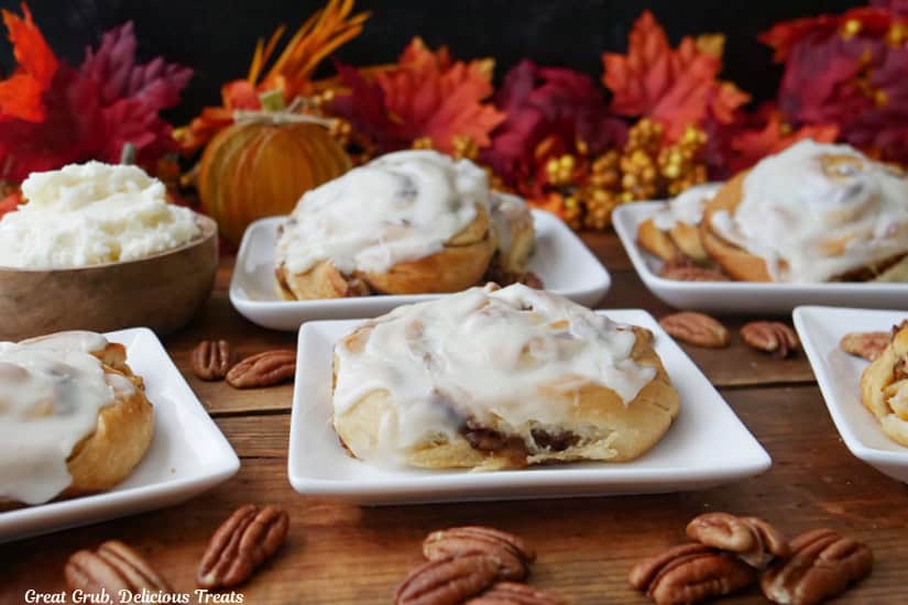 A wooden surface with six white square plate with pumpkin cinnamon rolls.
