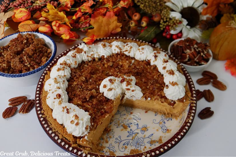 A pumpkin spice cream cheese pie in a deep dish pie dish with a couple slices removed and fall foliage in the background.