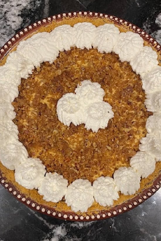 A pie dish with pumpkin cream cheese pie in it with homemade whipped cream piped around the edges.
