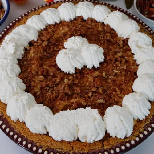 A round baking dish with a whole pumpkin cream cheese pie in it with whipped cream around the edges and in the middile.