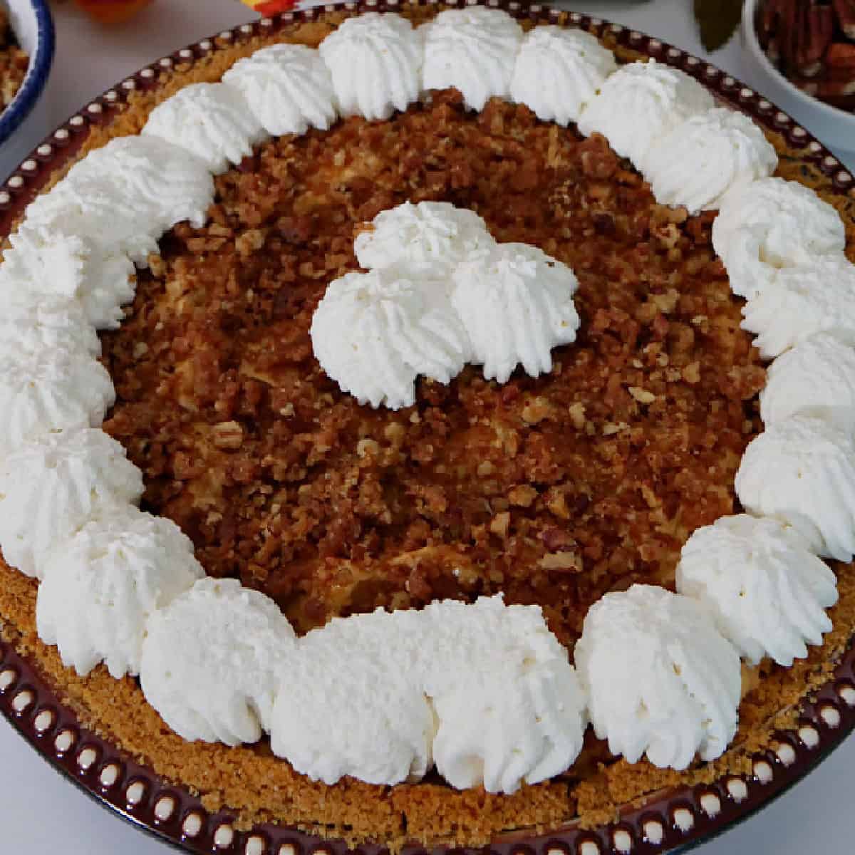 A round baking dish with a whole pumpkin cream cheese pie in it with whipped cream around the edges and in the middile.
