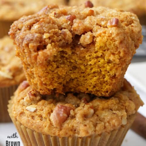 Two pumpkin muffins on top of each other with a bite taken out of the top muffin.