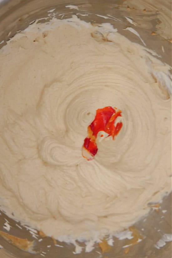 A mixing bowl with pumpkin mousse whipped together with a orange gel food coloring drops in it.