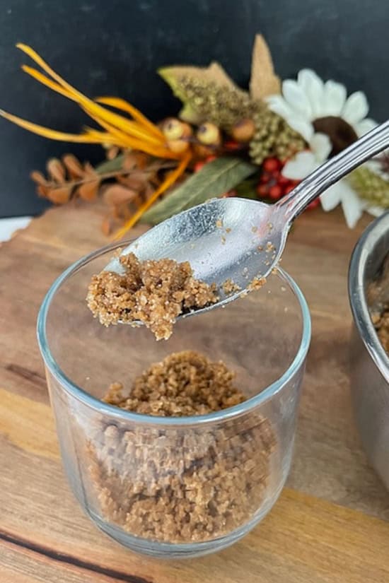 A wood surface with a glass cup and gingersnap crumbs added to the bottom on the cup.