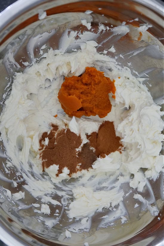 A silver mixing bowl with cream cheese, pumpkin puree and spices in it.