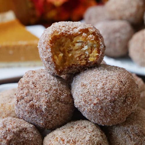 A stack of cinnamon sugar coated pumpkin pie balls on a white plate with a bite taken out of the one on top.