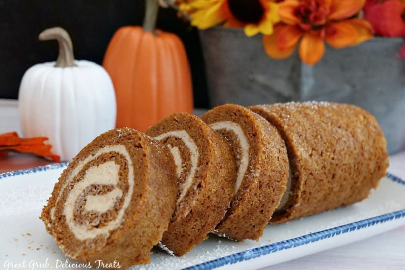 A white oblong plate with blue trim with a pumpkin roll that has been sliced placed on it.