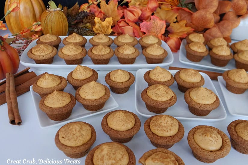 A white surface with 32 mini pumpkin spice cookie bites on it with fall foliage in the background.