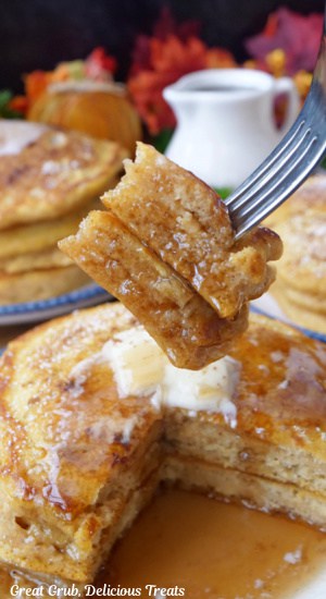 A bite of pancakes on a fork held above a plate with two pancakes on it.