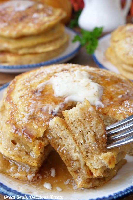 Three pancakes on a white plate with blue trim and a fork with a bite of pancakes on it.