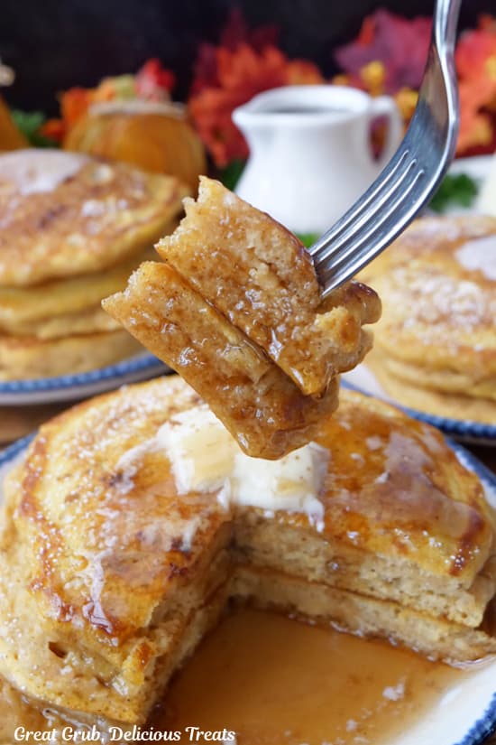 A bite of pancakes on a fork held up above the stack of pancakes.