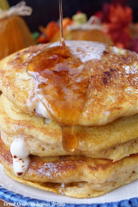 A stack of pumpkin spice pancakes with melted butter dripping down the side and syrup being pour on top.