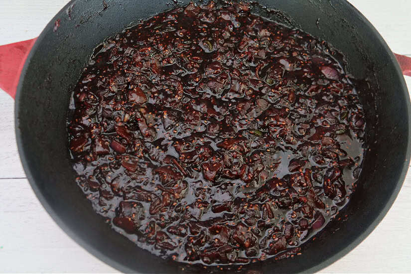 A white surface with a cast-iron skillet on it with raspberry jalapeno bacon jam in it.