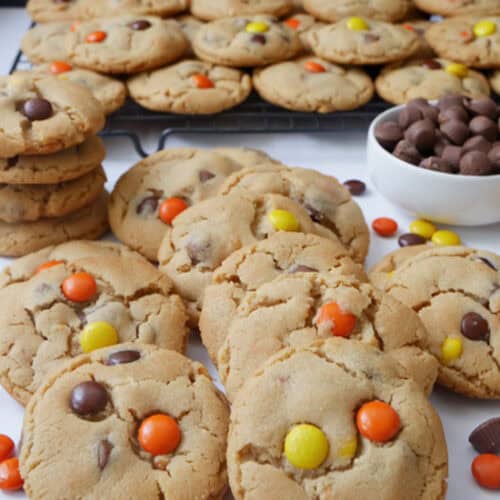 A white surface with a couple dozen peanut butter cookies on it and on a wire rack in the background.