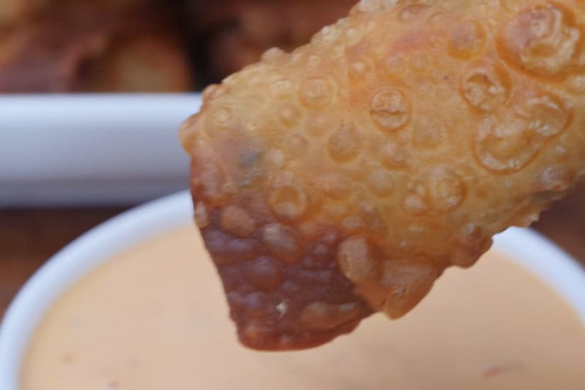 A fried Reuben egg roll being dipped in thousand island dressing.