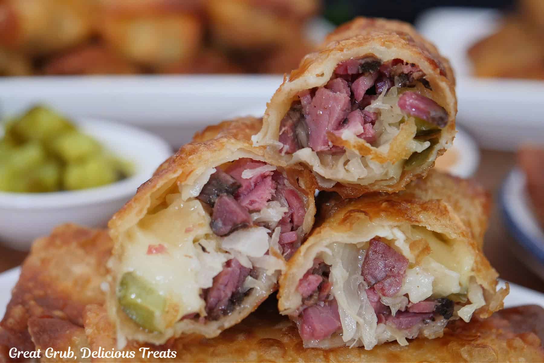 A stack of three Reuben egg rolls place on top of fried egg rolls showing the inside ingredients.