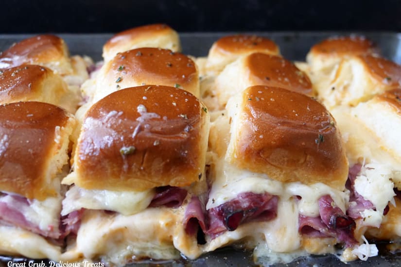 A horizontal photo of twelve Reuben sliders on a baking sheet after being removed from the oven.