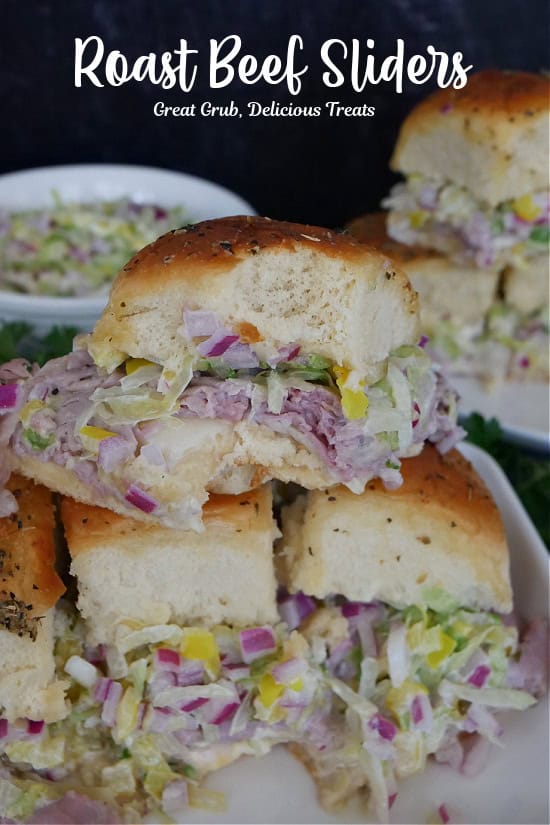 A few roast beef sliders on a white plate with a bite taken out of the slider on top.