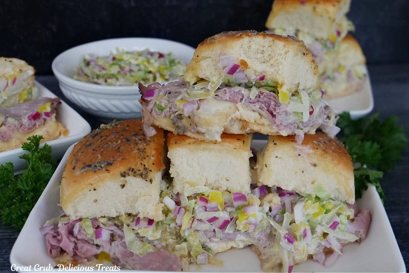 A white oblong plate with four roast beef sliders on it with more in the background.