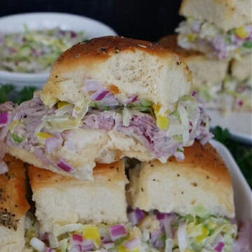 A white plate with four roast beef sliders on it with a bite taken out of the one on top.