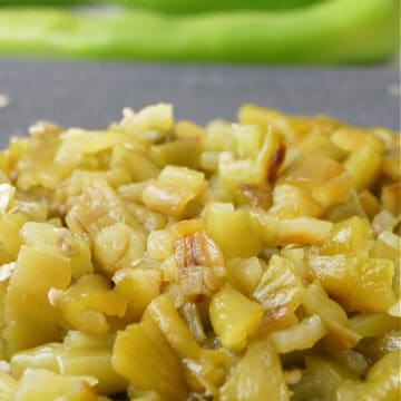 A black cutting board with diced Hatch chiles on it.