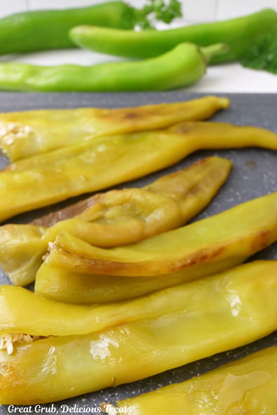 Six roasted hatch chiles on a black cutting board.