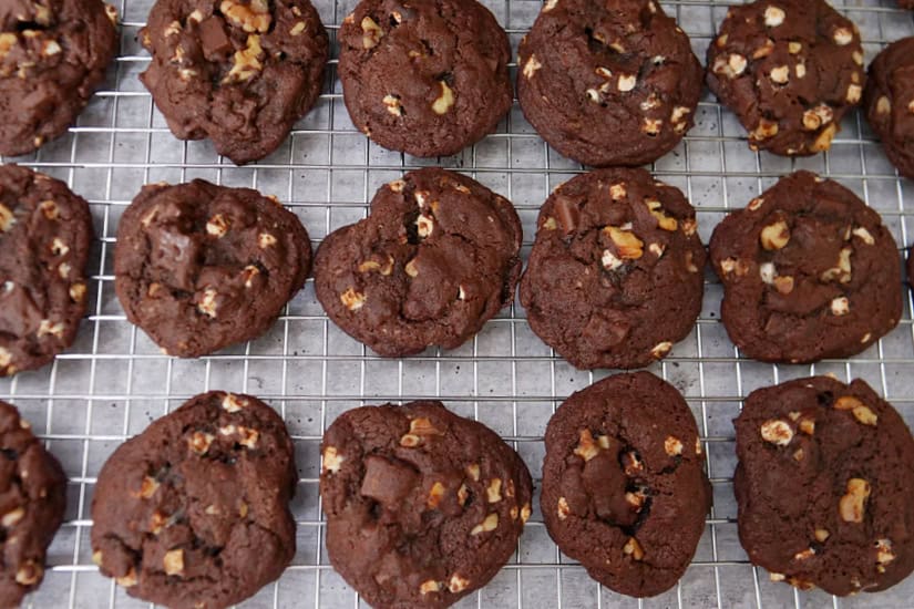 A wire rack with baked rocky road dark chocolate cookies on it.