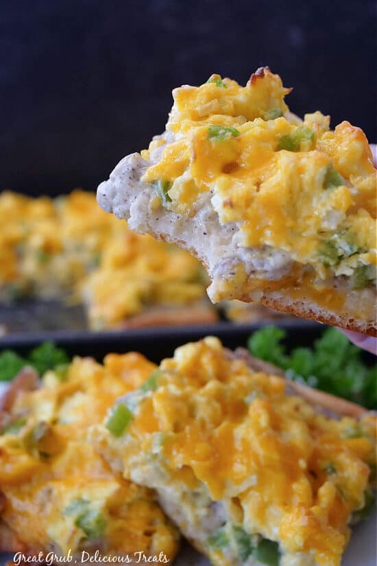 A close up of a slice of breakfast pizza with a bite taken out of it.