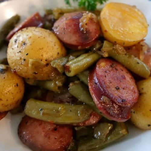 A white bowl with blue trim filled with kielbasa sausage, green beans, and baby creamer potatoes.