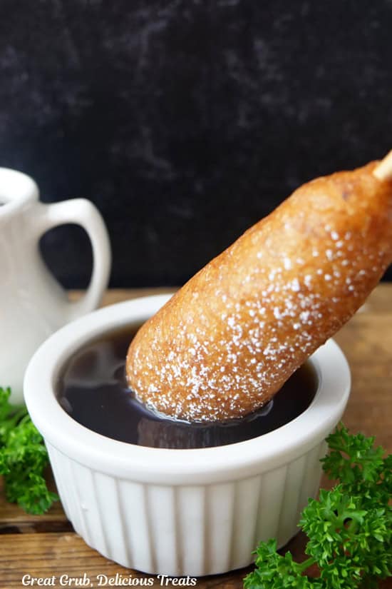 A pancake on a stick being dipped in a small white bowl filled with syrup.