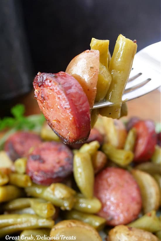 A bite of sausage, potato, and green beans on a fork.